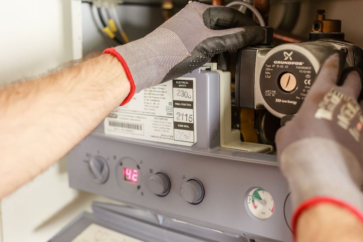 Gloved hands adjusting the pump inside a wall-hung gas boiler